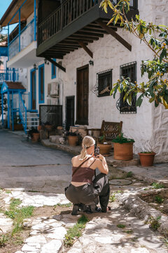 Young woman using smartphone in cozy Mediterranean cafe and garden courtyard, showing solo travel, vacation lifestyle, leisure, mobile connection and relaxed summer tourism.