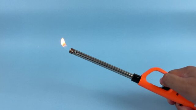Hand Holding Long Gas Lighter with Flame on Blue Background