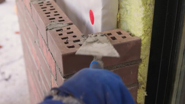 Bricklaying with precision. Builder aligning bricks carefully on wall surface. Detailed view of bricklayer securing brown bricks with precision and proper tools