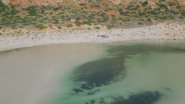 Drone aerial view of clear shallow turquoise water with dark underwater seaweed and algae growth along sandy shore at famous Balos lagoon in Crete island Greece