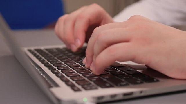 Coding hands work. Person in white sleeve entering commands on silver device. Detailed shot of hands typing code on modern laptop illuminated by soft studio lighting