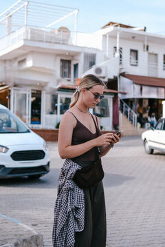 Young female traveler using smartphone outdoors, mobile travel planning, navigation and online booking during solo summer trip, modern connected travel lifestyle.