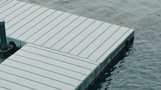 interlocking pale dock panels form diagonal corner above gently rippled teal water with small floating debris.