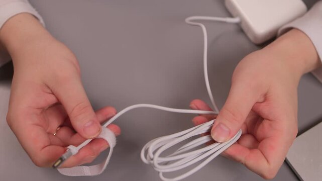 Cable tidying activity. Office worker carefully separating tangled electronic cables. Person methodically unravels knotted charging cables amid organized workspace setting