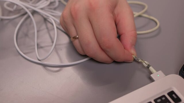 Laptop power cord repair process. Careful examination of frayed laptop connector wires. Closeup view of technician inspecting compromised power cable connections on desk