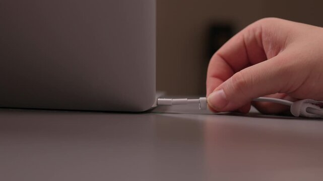 Laptop power cord repair process. Careful examination of frayed laptop connector wires. Closeup view of technician inspecting compromised power cable connections on desk