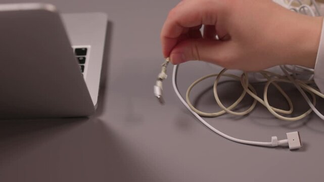 Laptop power cord repair process. Careful examination of frayed laptop connector wires. Closeup view of technician inspecting compromised power cable connections on desk