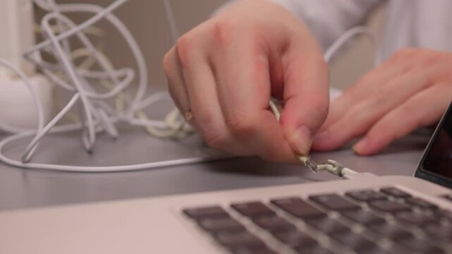 Laptop power cord repair process. Careful examination of frayed laptop connector wires. Closeup view of technician inspecting compromised power cable connections on desk