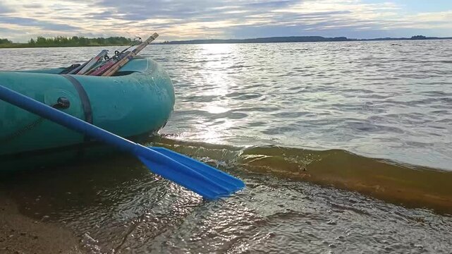 An inflatable boat with fishing rods stands on the shore of the lake.