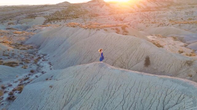 Cinematic Aerial View of Woman in Blue Dress Walking Through Desert Badlands at Sunset in Murcia Spain