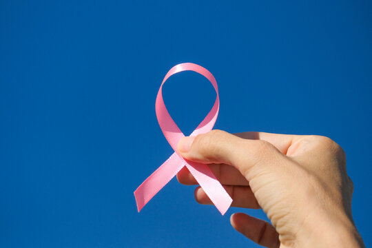 Pink breast cancer awareness ribbon held in woman hands against blue sky background in sunny day