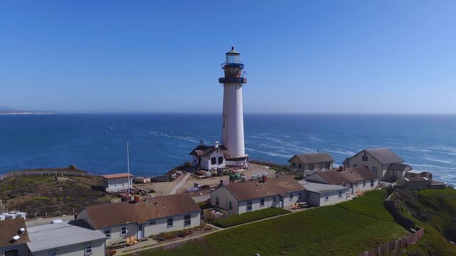 Aerial perspective of Pigeon Point Lighthouse standing tall on a rugged rocky headland along the Pacific Ocean coastline in California, surrounded by rolling coastal hills and ocean swells.