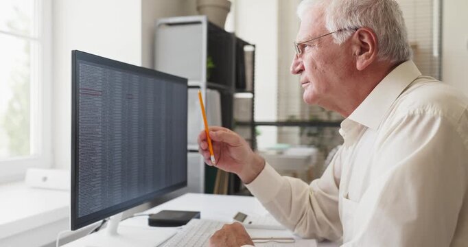 Senior man accountant analyst in office. He checks accounting analysis on computer, reviewing spreadsheet finance data and verifying numbers for accuracy. Clear finance analysis concept today.