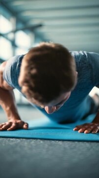 Focused young man performing push ups on a blue exercise mat in a modern gym environment. Intense workout session highlights strength, determination, and healthy lifestyle motivation