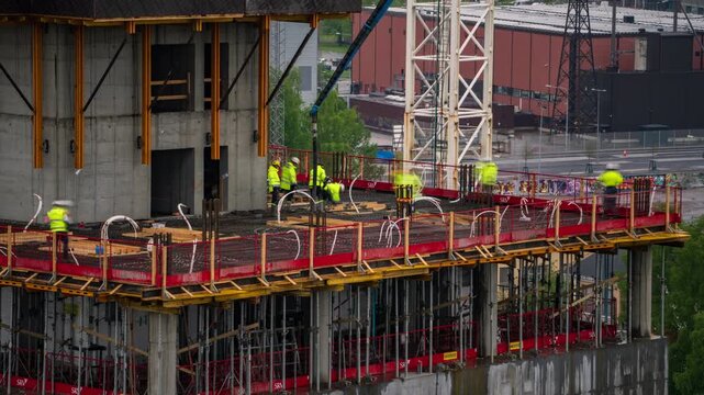 Helsinki, Uusimaa, Finland - 30 August 2022: View of construction workers in high-visibility jackets working on the Kalasatama high rise building site with cranes and scaffolding. Timelapse.