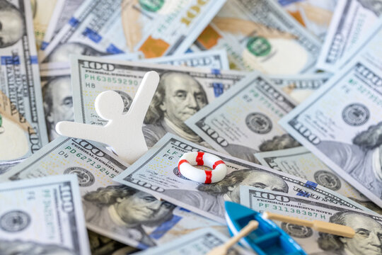Financial crisis survival and debt relief concept. Little wooden person falling overboard into money background near a small life ring.