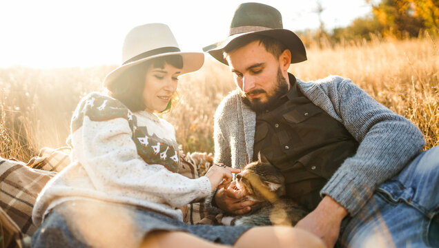Young couple spends time together sitting on blanket in field, petting a cat. Couple enjoys relaxing outdoors. Concept of love, enjoyment, and day off.
