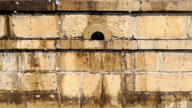 Weathered fountain wall features one dark outlet above stained stone blocks