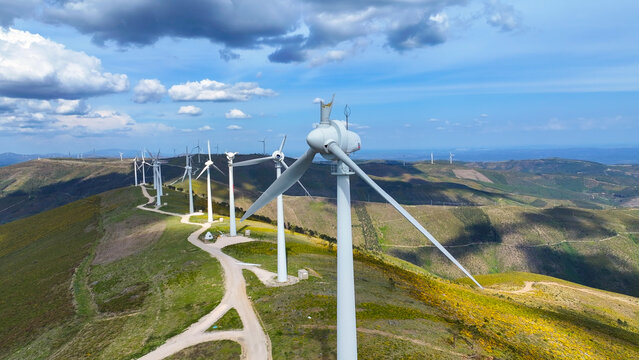 Aerial view of wind turbines on a hilly landscape with dirt roads under a blue sky in Lisbon, Lisbon, Portugal.