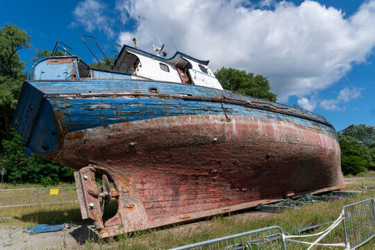 Large old wooden boat resting on dry land with heavily weathered blue and red paint, exposed timber and worn hull surface. Detailed maritime scene illustrates vessel restoration, deterioration, mainte