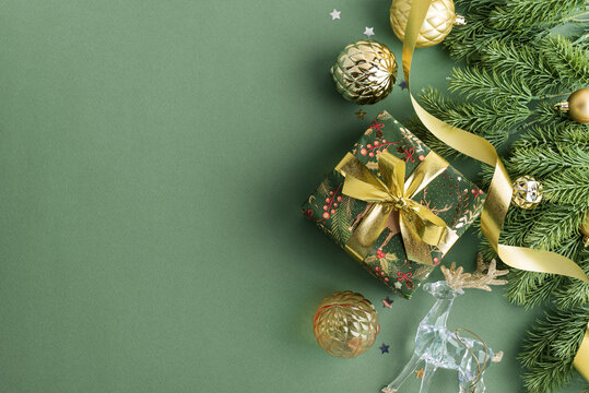 Festive Christmas gift box with ornaments ribbon pine branch reindeer on green background studio composition