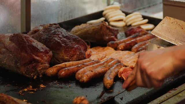 Chef hand turning roasted pork meat and chorizo sausages on flat griddle 60fps 4k