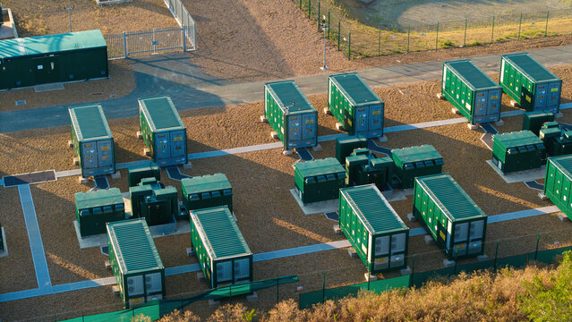 Aerial view of the Battery Energy Storage System at Grendon, featuring rows of green containerized battery units on a gravel site, enclosed by fencing in Northampton, England, United Kingdom.