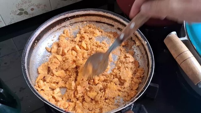 A hand manually stirring an egg and flour omelet in a metal pan