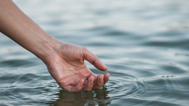 A person hand reaches into calm river water with soft natural light. Represents tranquility, mindfulness, and connection with nature for wellness and healing concepts.