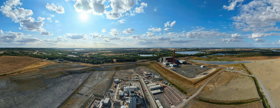 Aerial view of the Rookery South ERF and Millbrook power plant surrounded by industrial land, lakes, and open countryside under a bright blue sky in Stewartby, England, United Kingdom.