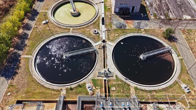 Different stages of wastewater treatment are shown with three circular tanks processing water at a facility in an urban area. Water flows and filtration methods are visible.
