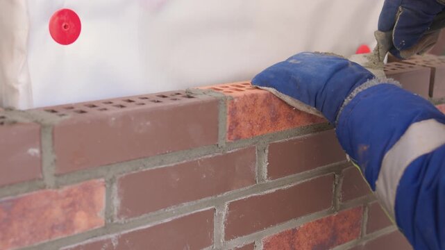 Bricklaying with precision. Builder aligning bricks carefully on wall surface. Detailed view of bricklayer securing brown bricks with precision and proper tools