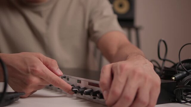 Technician finetunes audio equipment. Sound technician carefully calibrates audio device using tactile analog interface under warm ambient lighting in modern studio setting