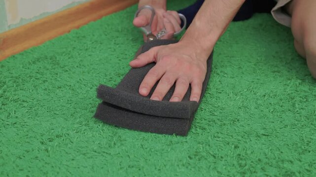 Cutting and shaping acoustic foam for soundproofing purposes. Meticulously trimming black foam with utility knife to ensure snug fit around baseboards and flooring edges