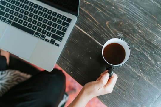 Person working on a laptop while holding a cup of coffee on a dark wooden table