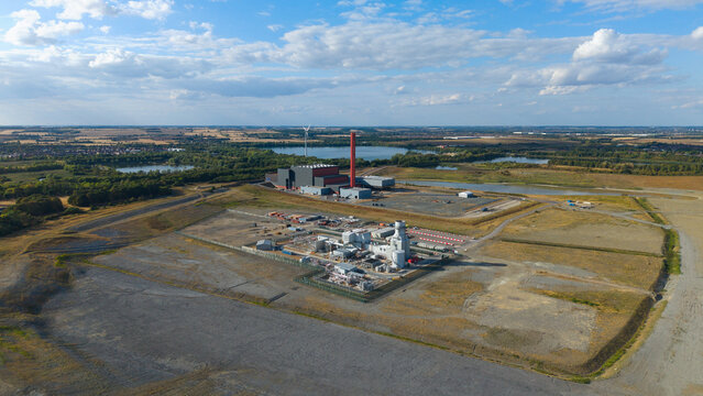 Aerial view of Millbrook Power Plant featuring its prominent red chimney and industrial infrastructure set within a landscape of fields and lakes in Stewartby, England, United Kingdom.