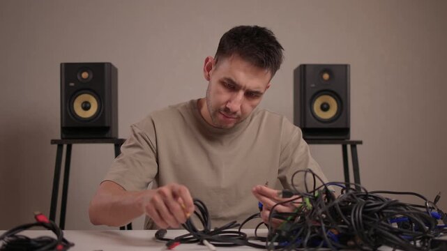 Focus on meticulous cable management in recording studio environment. Detailed image of audio technician systematically coiling cables with monitor speakers in backdrop