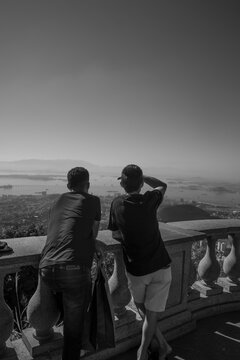Dos j&oacute;venes de espaldas en un mirador contemplando una amplia bah&iacute;a urbana