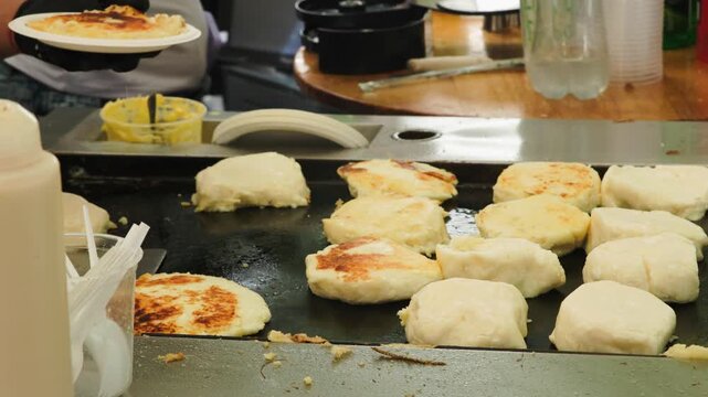 Side view wide shot of cook hand flipping traditional Colombian Venezuelan cheese corn cakes arepas on griddle 60fps 4k