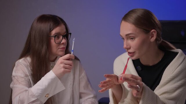 Caucasian women demonstrating brushing methods. Two women explain oral hygiene in studio setting. Women showcase proper tooth brushing techniques with educational intent
