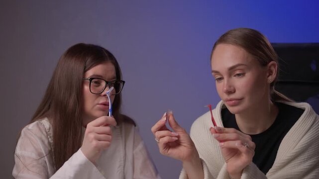 Caucasian women demonstrating brushing methods. Two women explain oral hygiene in studio setting. Women showcase proper tooth brushing techniques with educational intent
