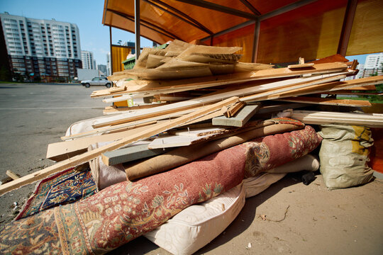 Close up overview of discarded wooden planks, old carpets, mattresses, and scrap materials piled under a canopy at a residential waste collection point