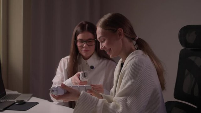 Caucasian women assess smart socket functionality carefully. Two ladies of Caucasian descent collaboratively inspect and compare smart socket models on studio desk