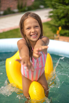 A cheerful, mischievous, laughing girl is swimming in an inflatable pool in the yard.