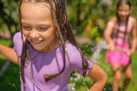Close‑up portrait of a happy, laughing girl in splashes of water. Hot, sunny summer day.