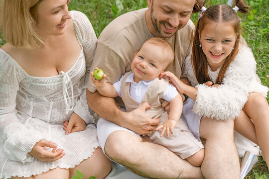 A portrait of a happy young family with two children. A little boy is nibbling on an apple while sitting in his father&rsquo;s arms.