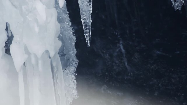Sharp icicle dripping over dark rock. Close up frozen cave wall ice formation.