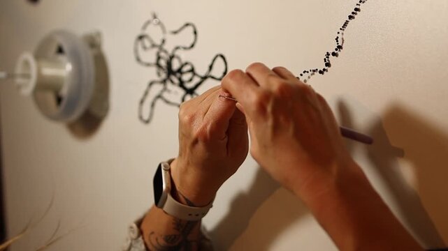 Mid shot of a woman working on a modern wall art installation, crocheting with black thread and beads on a white background. Creative handmade process, contemporary craft.