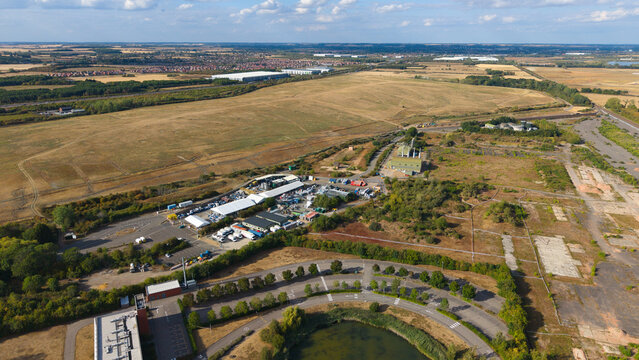 Aerial view of an industrial site with a parking lot, storage facilities, and surrounding open fields in Stewartby, England, United Kingdom.