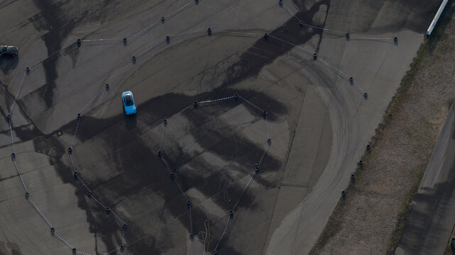 Aerial view of a blue car driving on a paved test track marked with tires and white lines in Hockenheim, Baden-Wurttemberg, Germany.